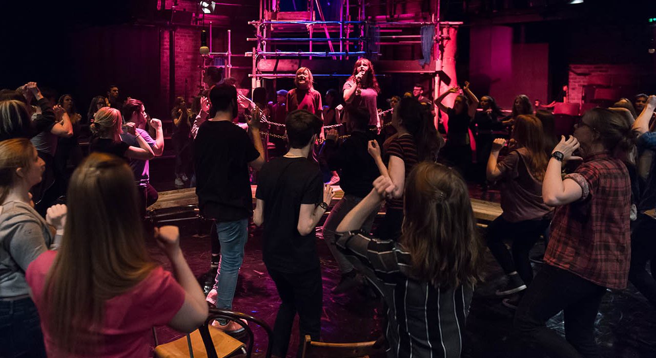 Two people in the center shouting at a crowd of the cast