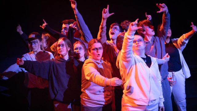 A group of 14 - 17 year olds on stage with their arms up in the air