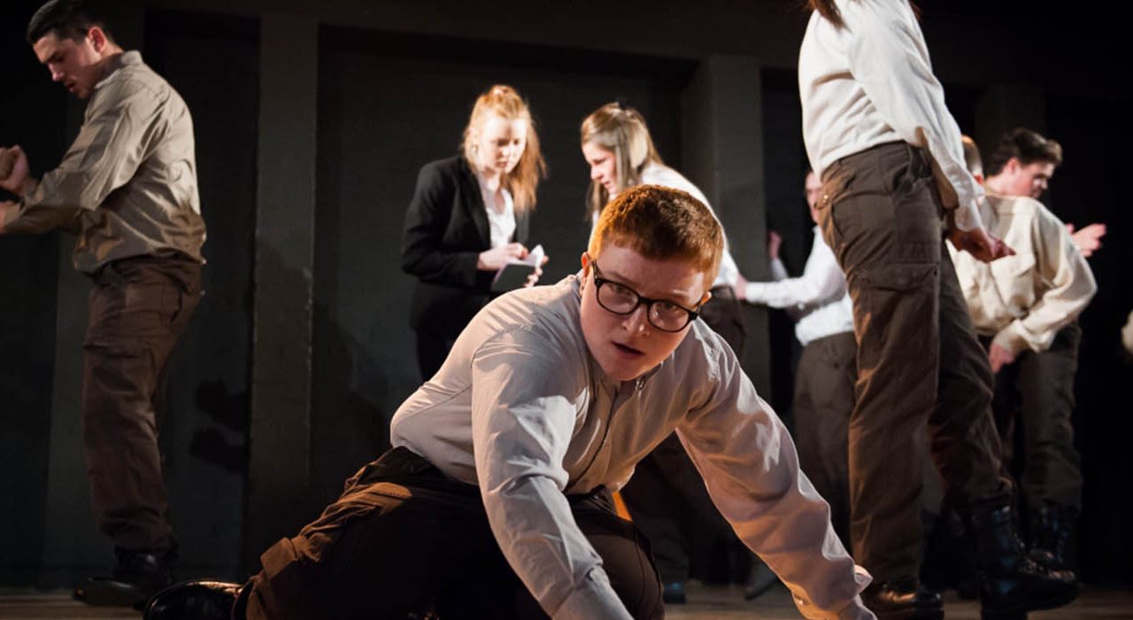 A person on the ground feeling the floor. In the background are other people wearing office outfits.