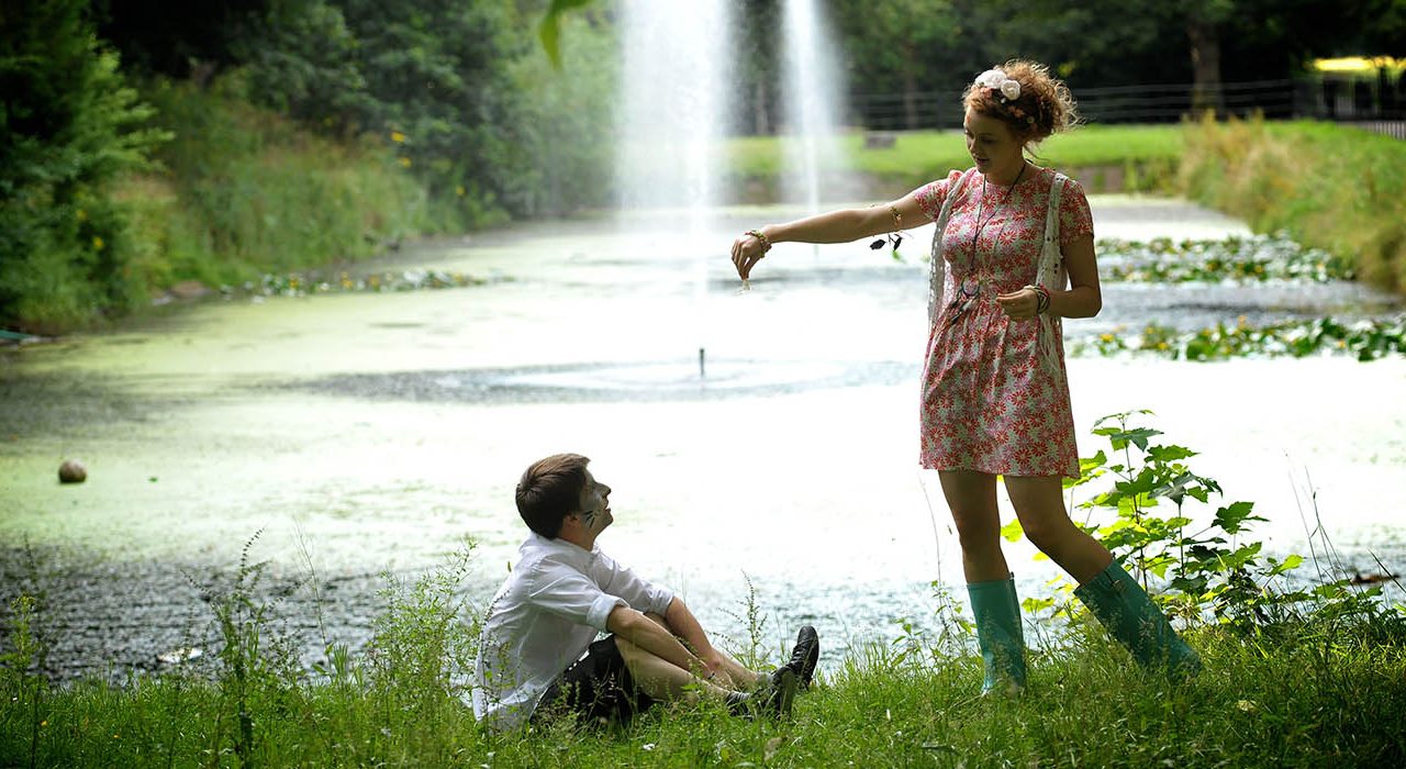 Two people with animal face paint on in a park next to a body of water