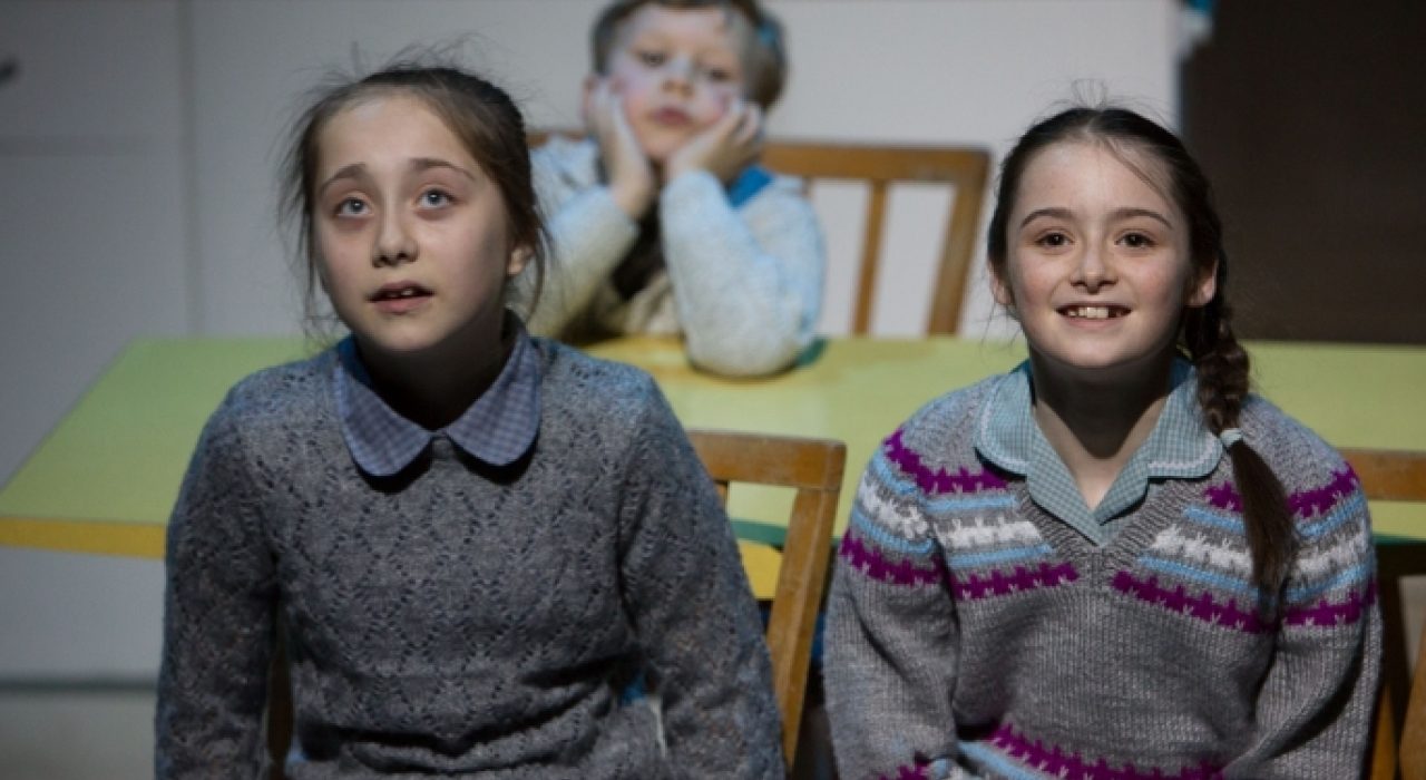 Two young girls in grey cardigans sat at a table