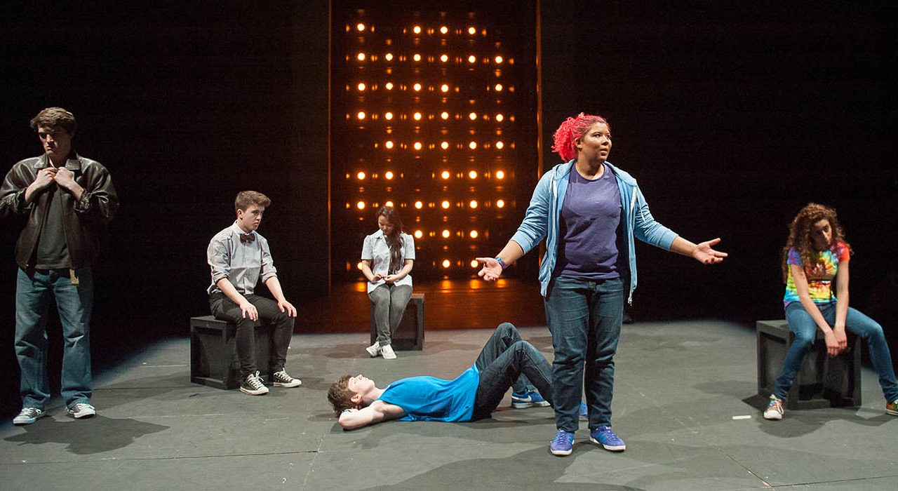 Two people stood infront of 3 people sat on blocks and a person lying on the floor.