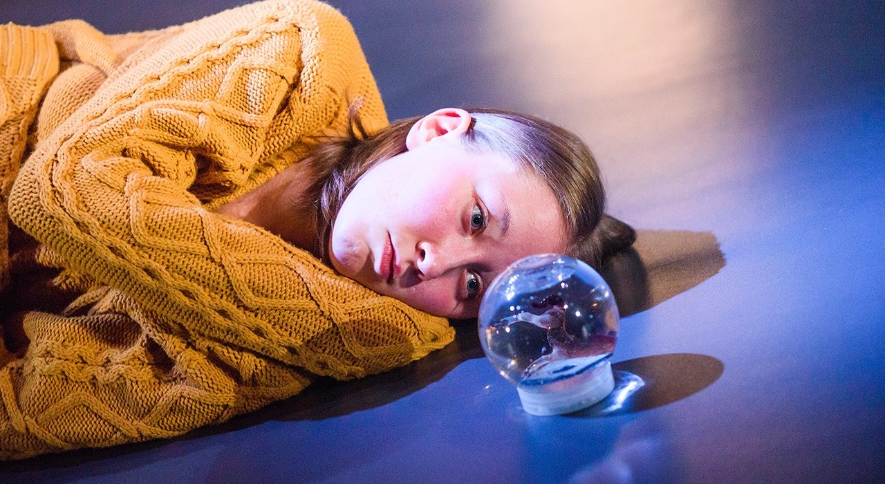 A girl lying on the floor taring at a snow globe