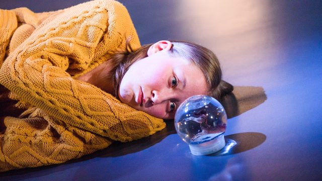 A girl lying on the floor taring at a snow globe