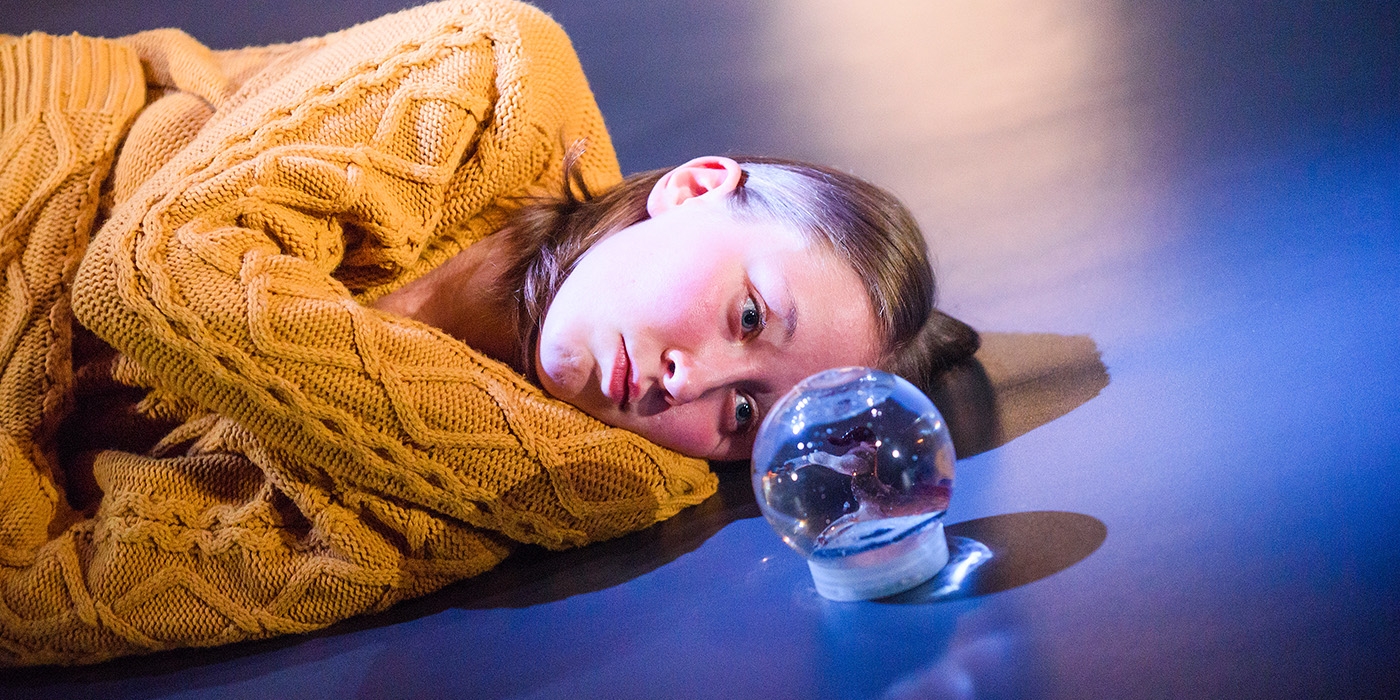 A girl lying on the floor taring at a snow globe