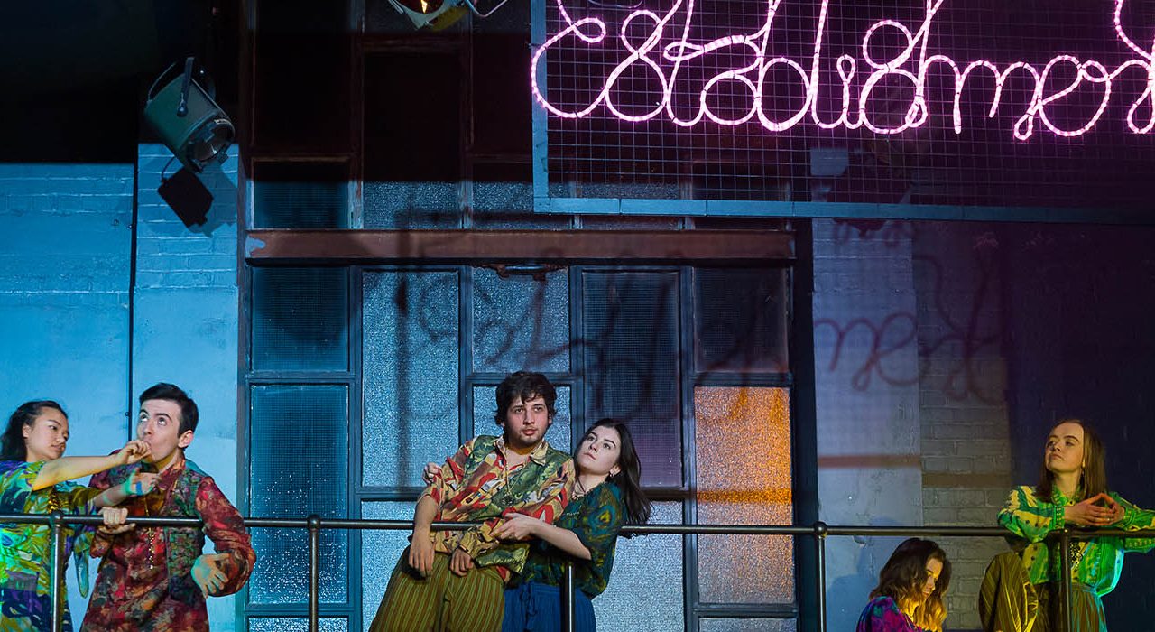 A person wearing green shirt and a person wearing a floral top stood on a bannister. Theres two more couples dressed the same