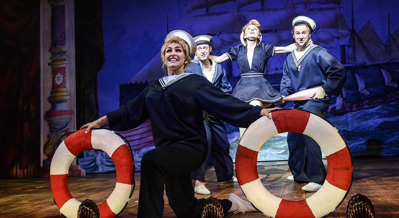 Four people dressed as sailors. One is holding two buoyancy rings