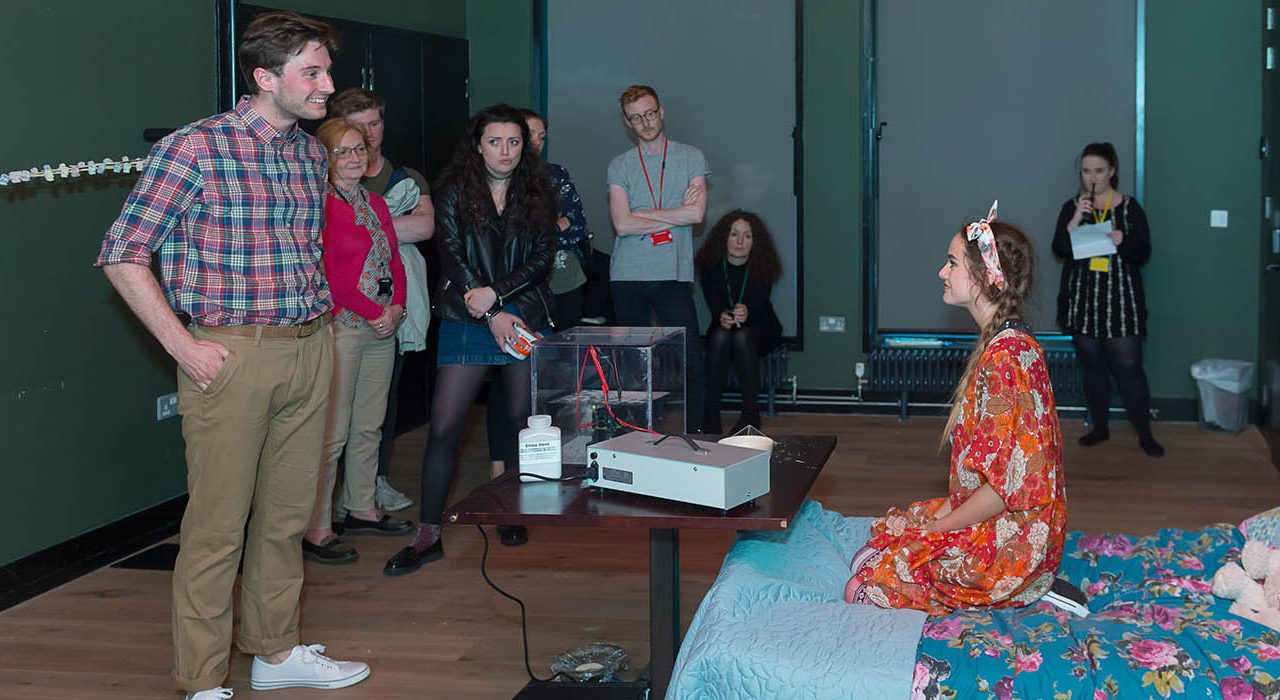 A crowd interacting with a woman on a bed