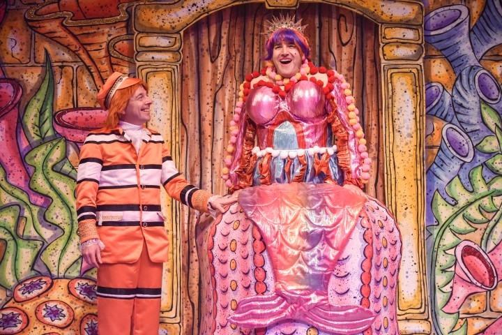 Two people in brightly coloured outfits. Ones wearing a clown fish print suit and the other in an elaborate pink dress