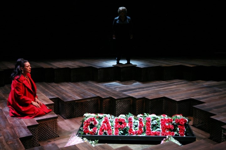 A woman kneeling on the floor wearing all red next to a flower display that says 'capulet'