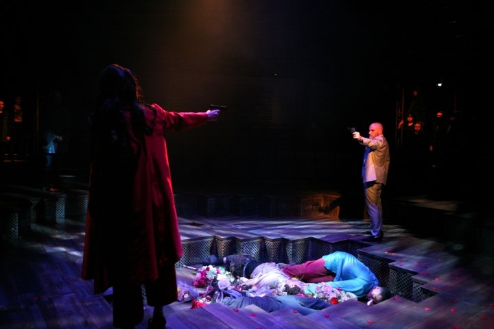 Two people pointing guns at eahother over a pit with two bodies in