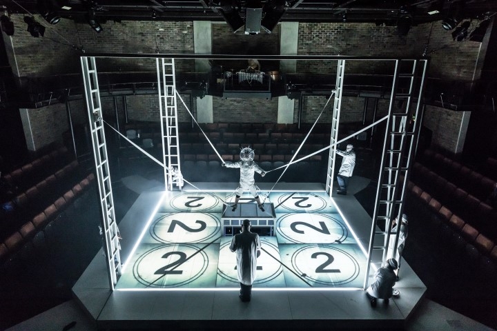 A stage set like a box with scaffolding and light projections of the number 2 on the floor