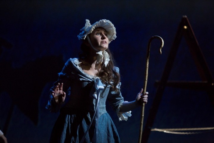 A woman dressed in a blue dress and bonnet. She is holding a shepards crook