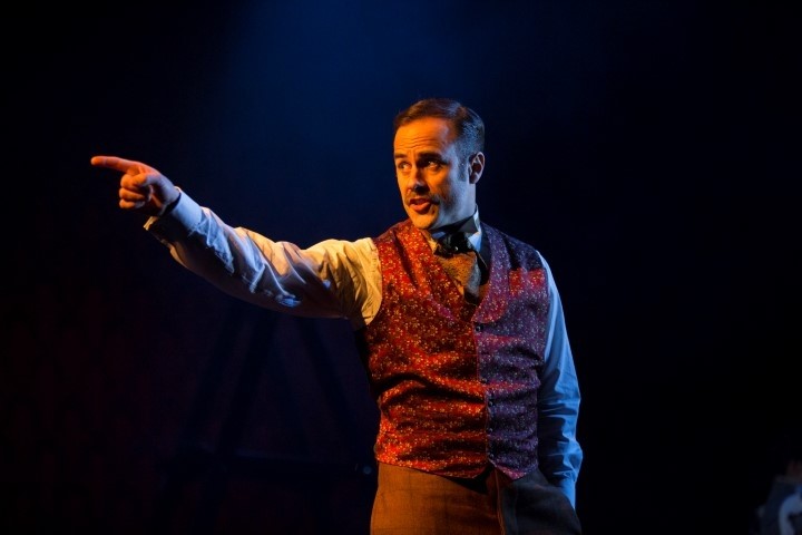 A man pointing wearing a red waist coat and neckerchief.