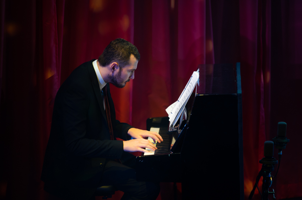 A man hunched over at a piano, playing an dreading the sheet music