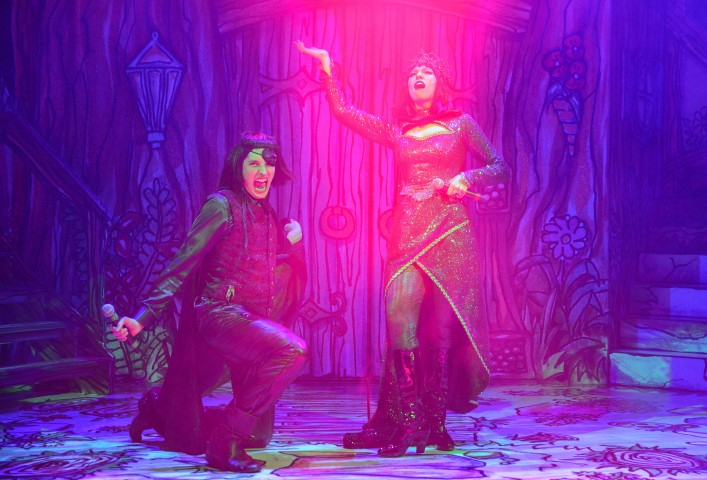 two people with green skin in all back dresses and boots stood singing.