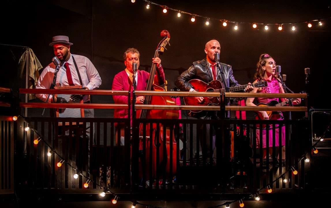 A four piece live band containing a musical wash board, cello, an acoustic and electric guitar