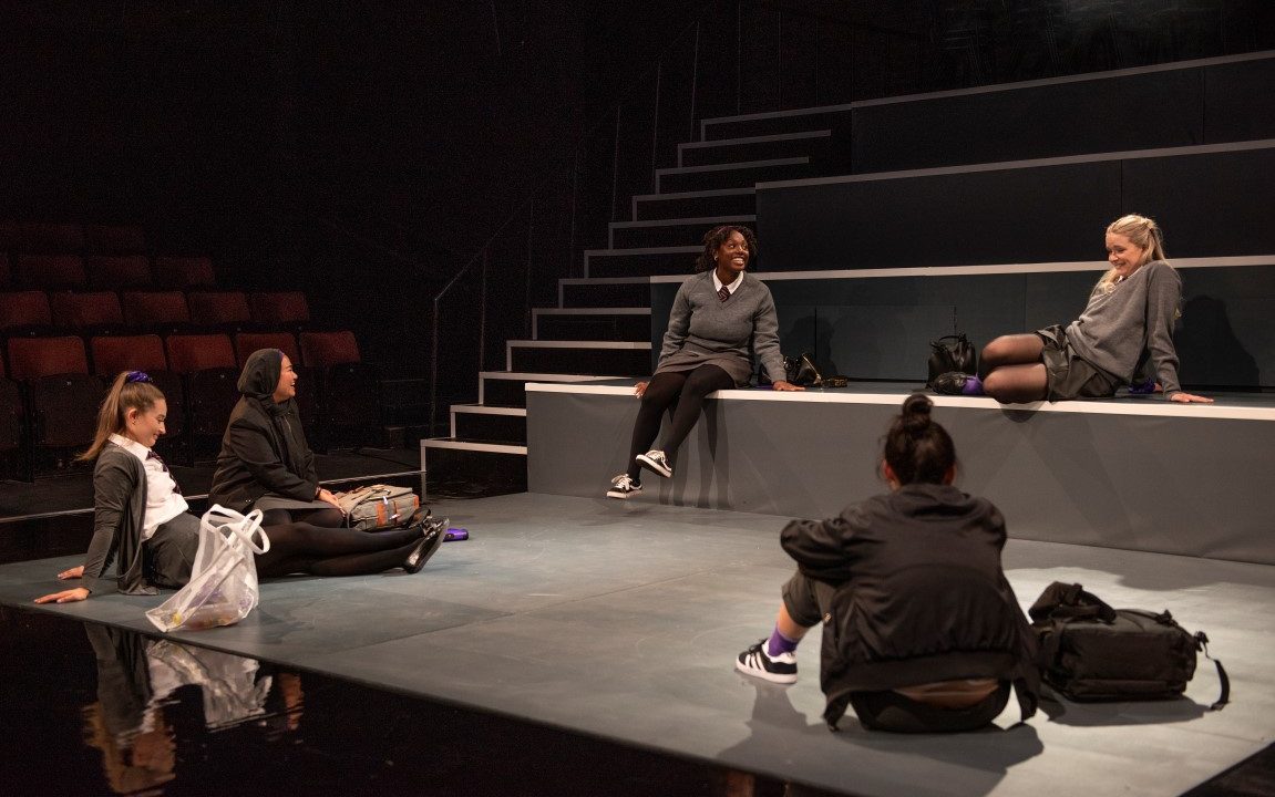 Five girls dressed in grey school uniform sat in a circle