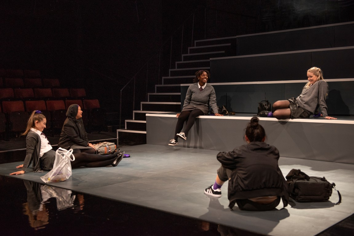 Five girls dressed in grey school uniform sat in a circle