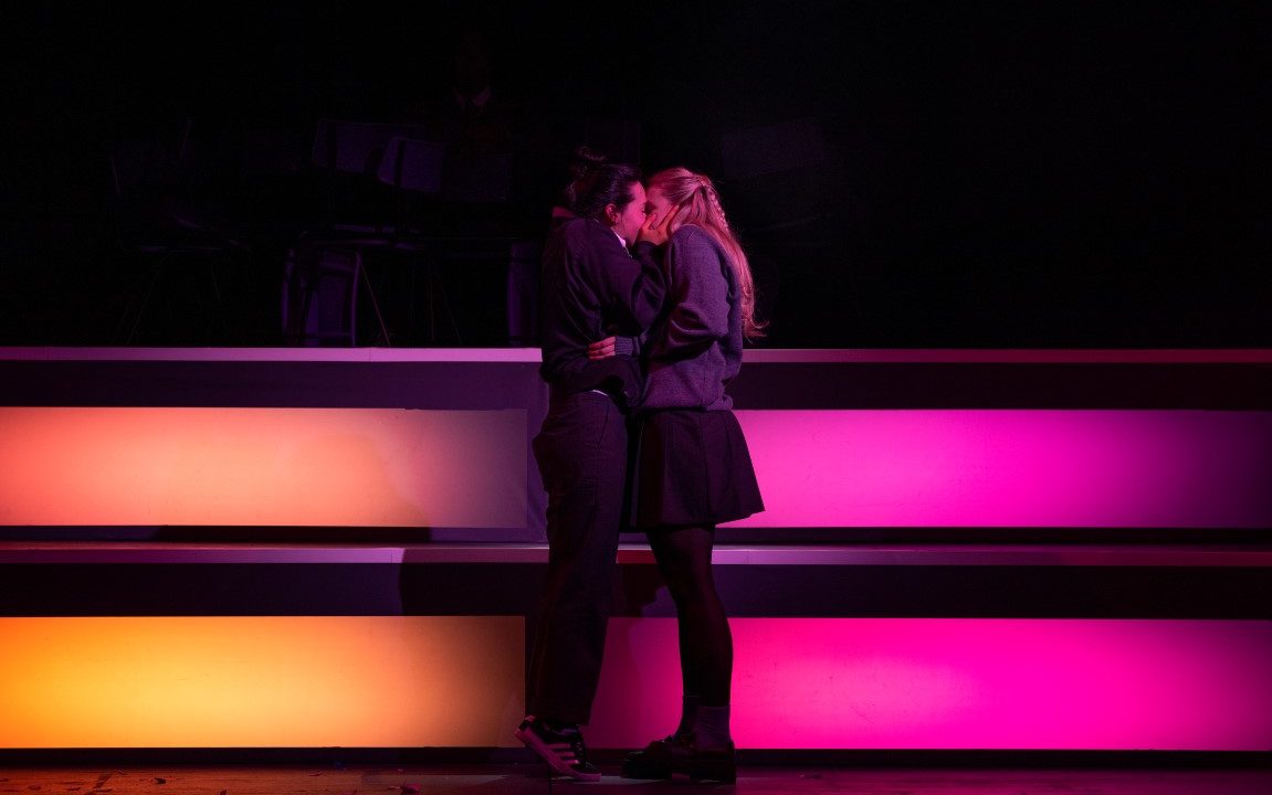 Two girls in grey school uniforms kissing.