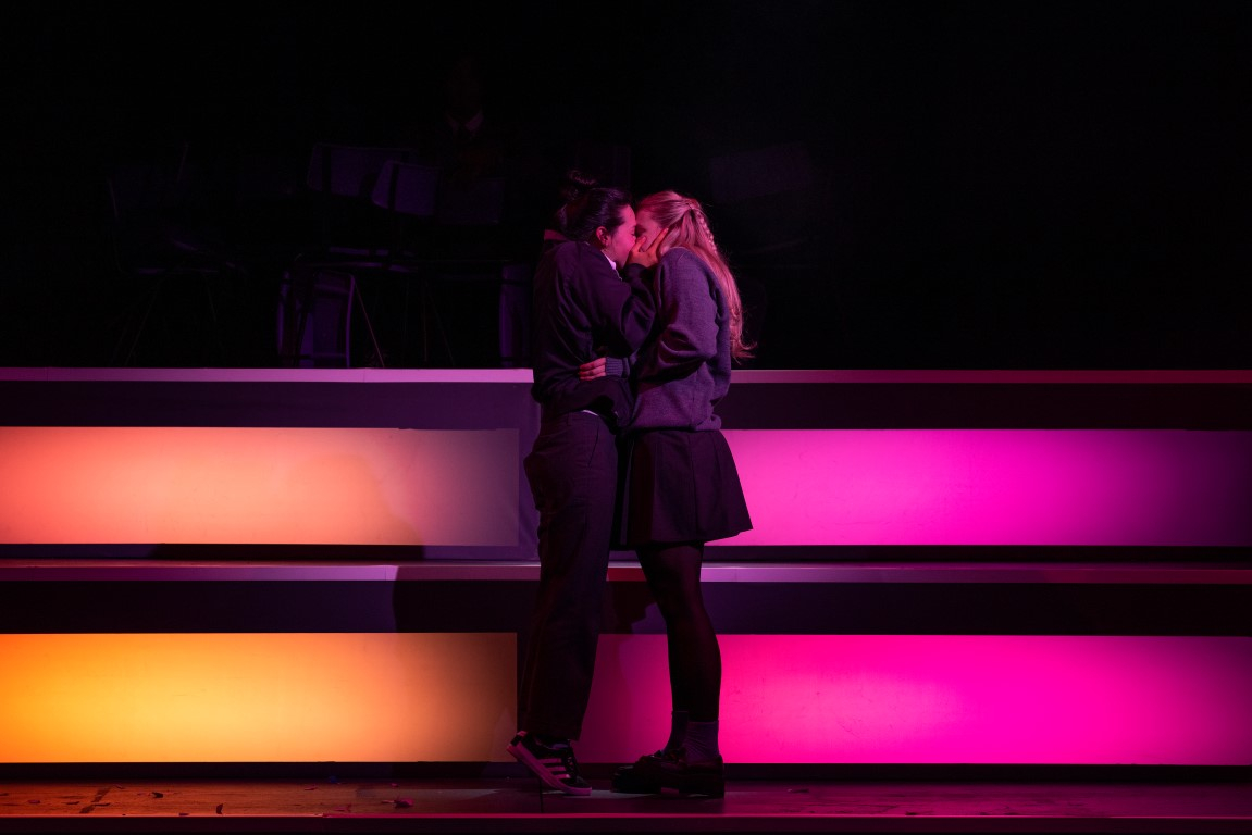 Two girls in grey school uniforms kissing.