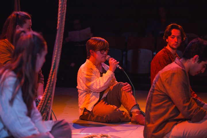 A man sat holding a microphone, with 4 people sat around them.