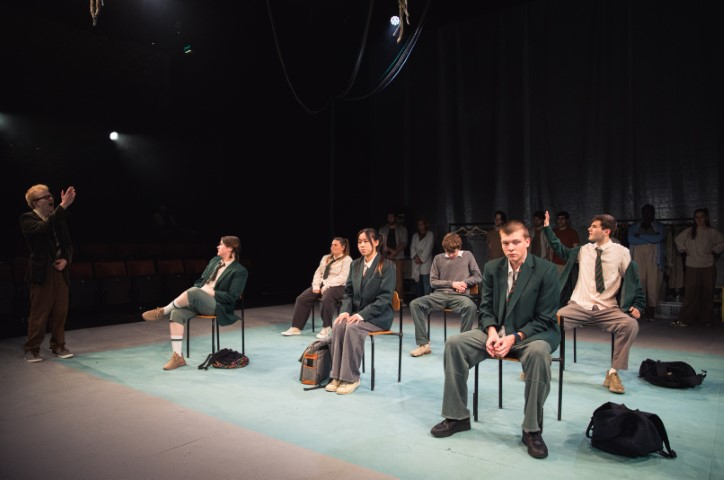 six people sat on chairs in two rows wearing school uniforms