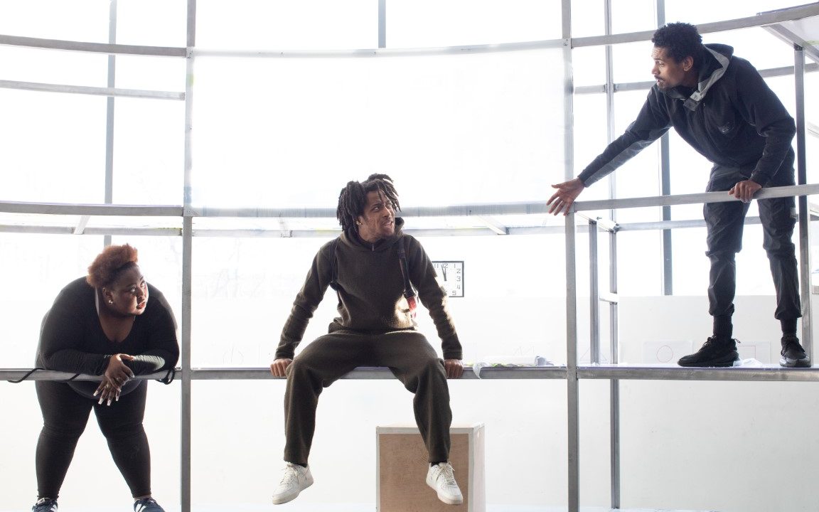 Three people in all black outfits sat on scaffolding