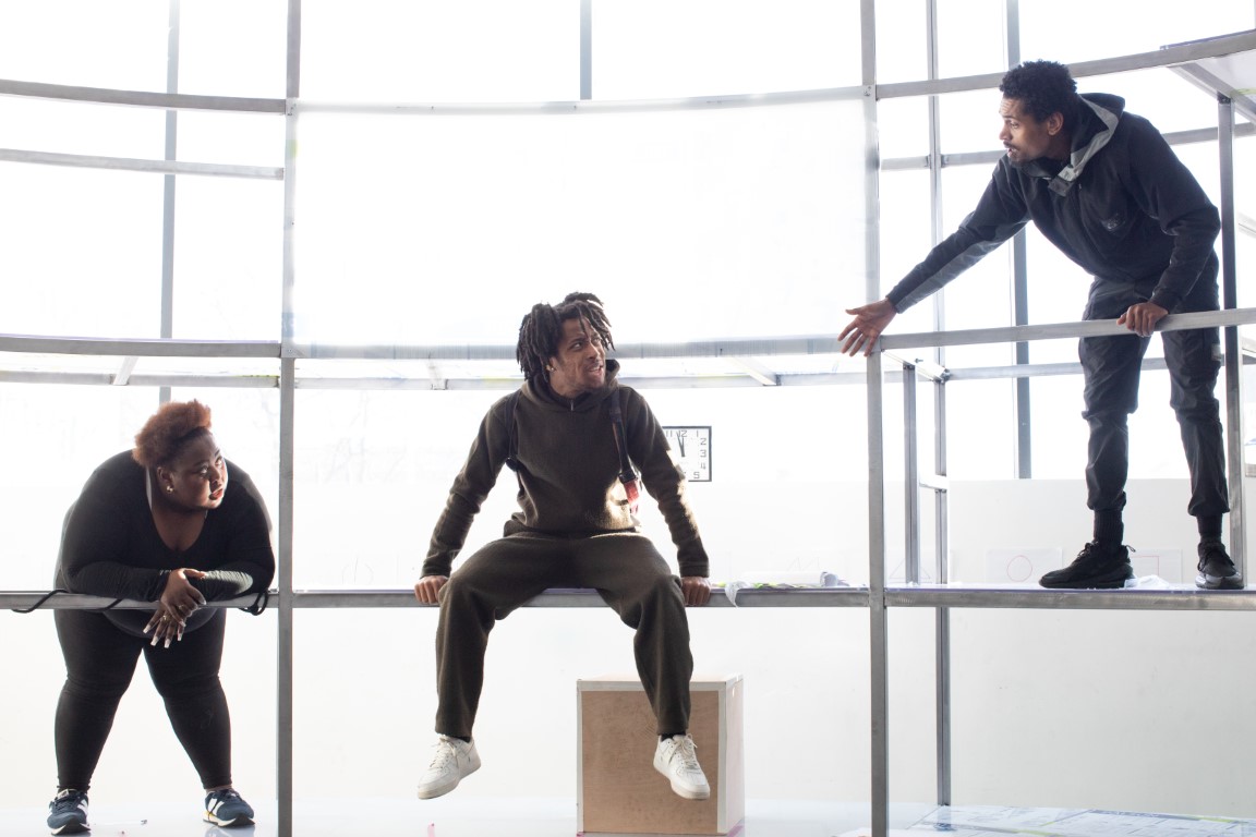 Three people in all black outfits sat on scaffolding