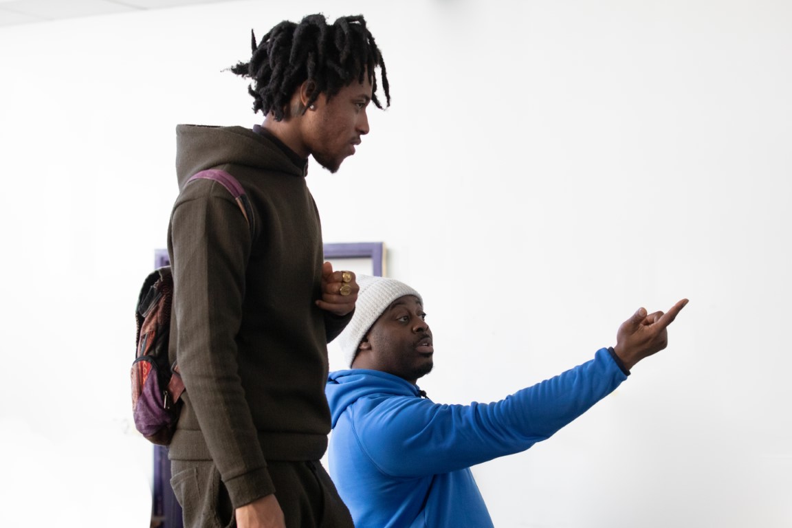 A person in a blue hoodie and white beanie pointing. Another person is looking where they are pointing